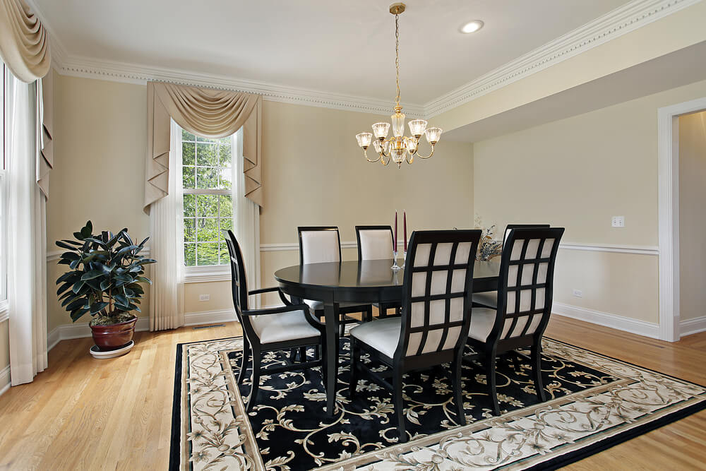 Formal dining room with very light beige walls, white ceiling and trim and light wood floor. Black dining table with six black and white dining chairs match the black, beige and white rug