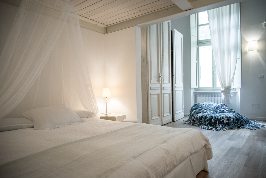 Via delle Orfane by CON3STUDIO - Small Pillows On Bed Added Near Glass Windows On Wall Decor