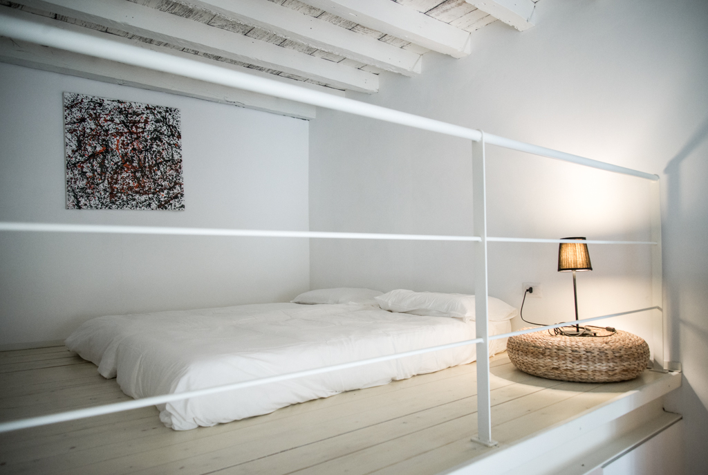 Via delle Orfane by CON3STUDIO - White Bed Land On Floor Added Near Desk Lamp On Round Shaped Table